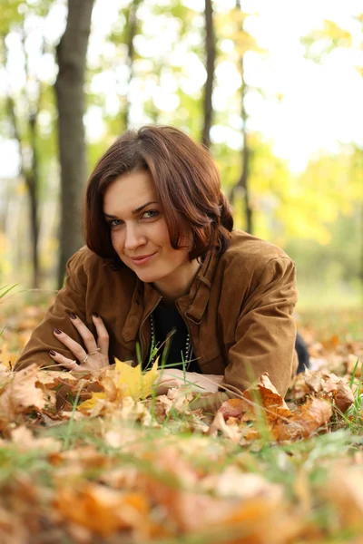 Жінка лежить на килимі листя в осінньому парку — стокове фото
