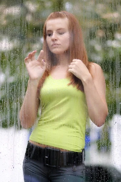 Jeune femme regardant par la fenêtre en verre — Photo