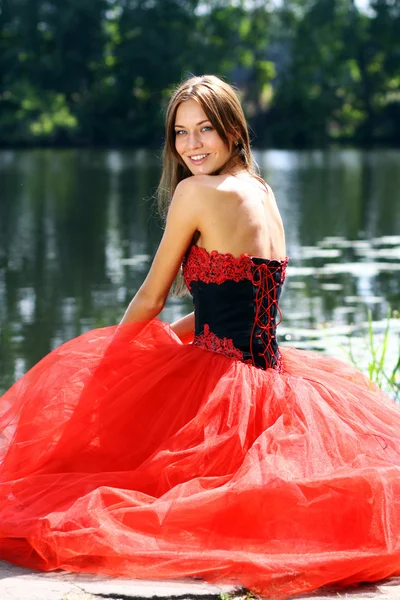 Glimlachende vrouw in een rode jurk zittend in de buurt van rivier — Stockfoto