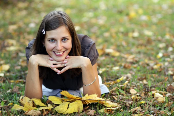 Vrouw liggend op een tapijt van bladeren in de herfst park — Stockfoto