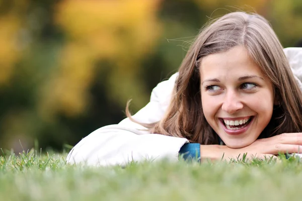 Vrouw liggend op een tapijt van bladeren in de herfst park — Stockfoto