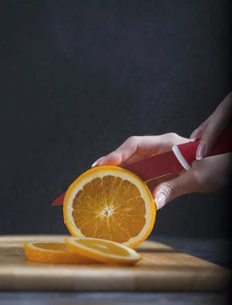 Woman's hands cutting fresh orange on kitchen — Stock Photo, Image