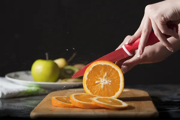 Woman's hands cutting fresh orange on kitchen — Stock Photo, Image