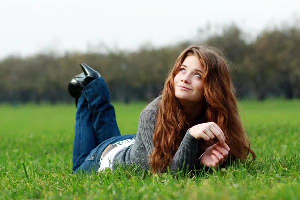 Vrouw liggend op een tapijt van bladeren in de herfst park — Stockfoto