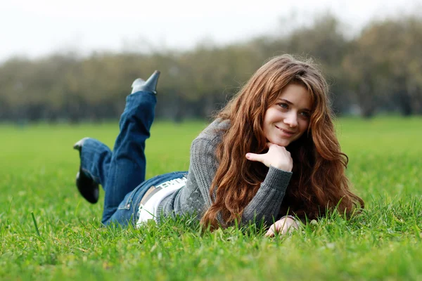 Vrouw liggend op een tapijt van bladeren in de herfst park — Stockfoto