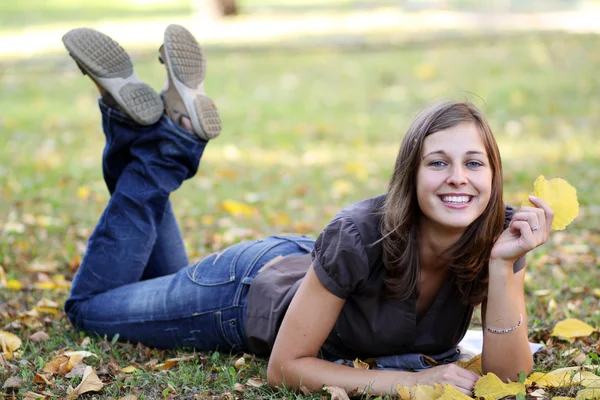 Vrouw liggend op een tapijt van bladeren in de herfst park — Stockfoto