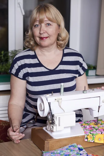 Old woman sews on the sewing machine — Stock Photo, Image