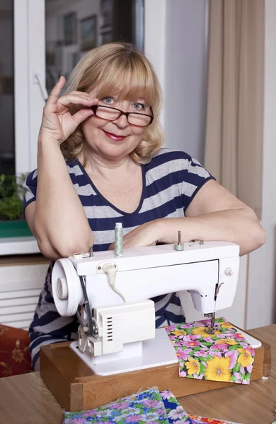 Old woman sews on the sewing machine — Stock Photo, Image