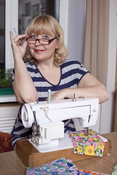 Old woman sews on the sewing machine — Stock Photo, Image