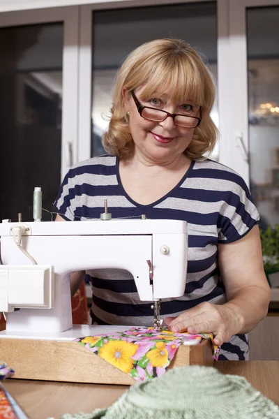 Old woman sews on the sewing machine — Stock Photo, Image