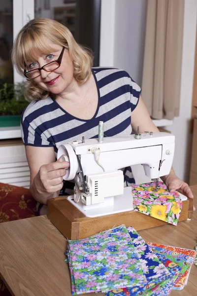 Old woman sews on the sewing machine — Stock Photo, Image