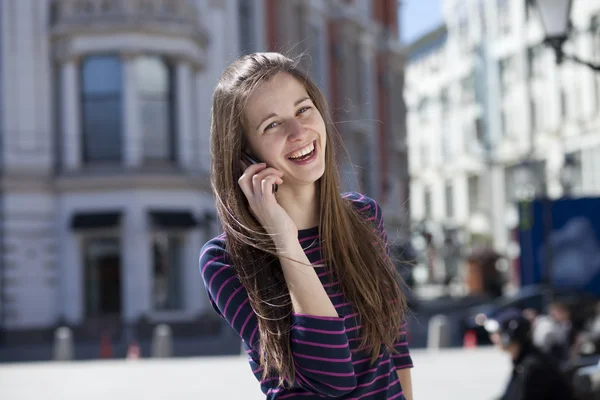 Mladá šťastná žena volá po telefonu na ulici — Stock fotografie