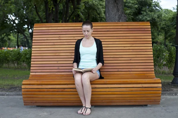 Morena sentado em um banco em um parque de verão — Fotografia de Stock