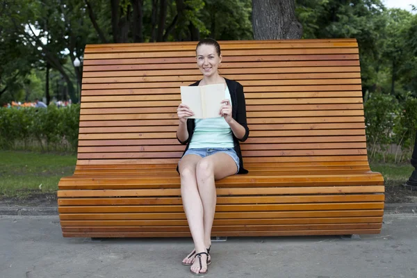 Brunette sitting on a bench in a summer park — Stock Photo, Image