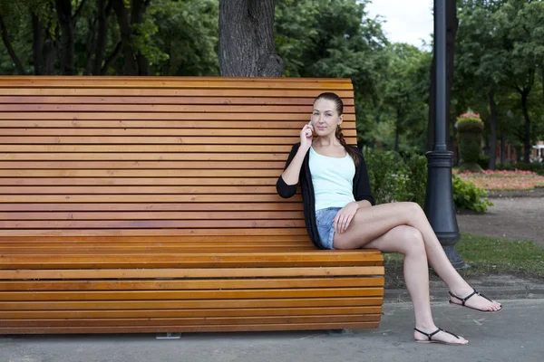 Morena sentado em um banco em um parque de verão — Fotografia de Stock