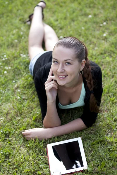 Mujer joven acostada en la hierba con el teléfono en la mano —  Fotos de Stock