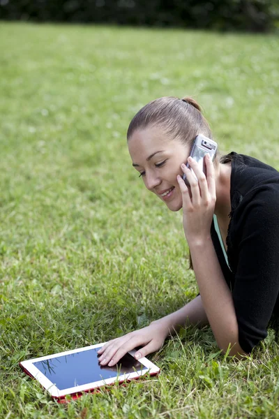 Ung kvinna liggande på gräset med telefonen i handen — Stockfoto