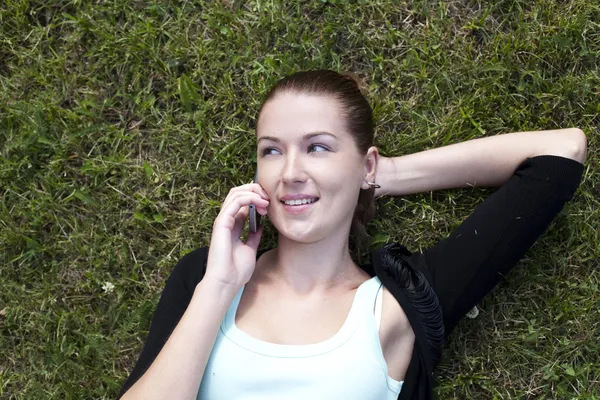 年轻女子躺在草地上，用手机在手 — 图库照片