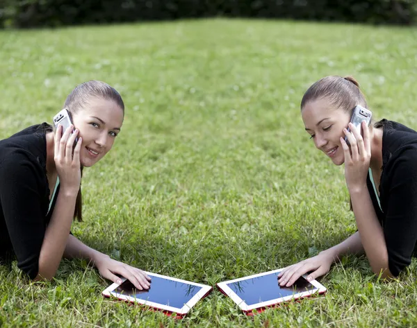 Mujer joven acostada en la hierba con el teléfono en la mano — Foto de Stock