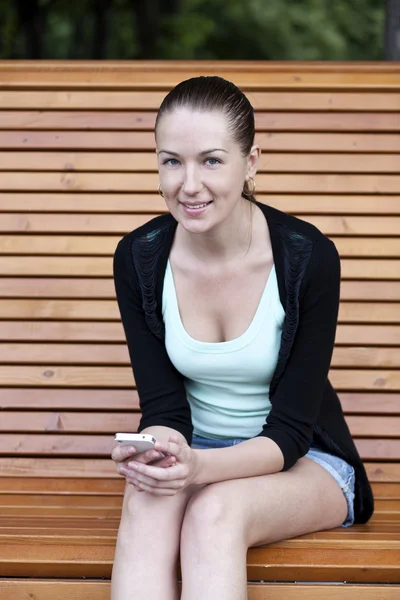 Brunette zittend op een bankje in het park van een zomer — Stockfoto