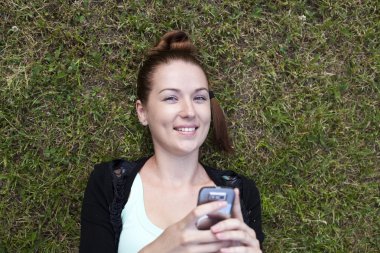 genç bir kadın elinde telefon ile çim üzerinde yalan