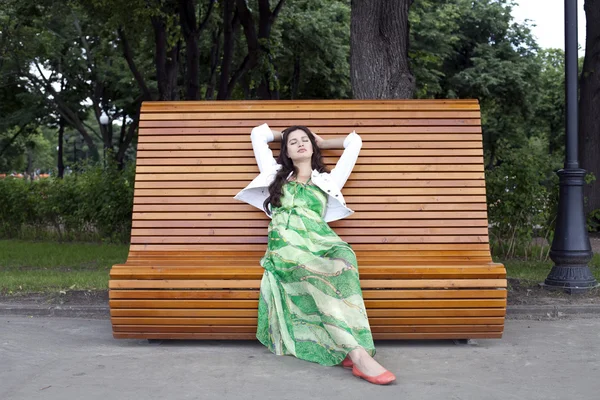 Bruneta sedí na lavičce v parku letní — Stock fotografie