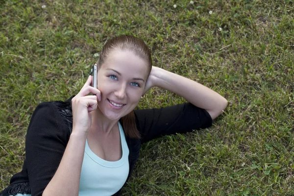 Genç bir kadın elinde telefon ile çim üzerinde yalan — Stok fotoğraf