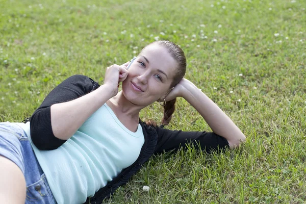 Junge Frau liegt mit Handy in der Hand im Gras — Stockfoto