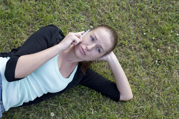 Jonge vrouw liggen op het gras met telefoon in de hand — Stockfoto