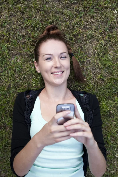 Mladá žena ležící na trávě s telefonem v ruce — Stock fotografie