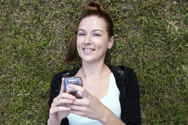 Mladí womanl, ležící na trávě s telefonem — Stock fotografie