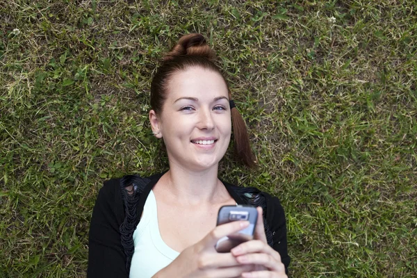 Молодая женщина лежит на траве с телефоном в руке — стоковое фото