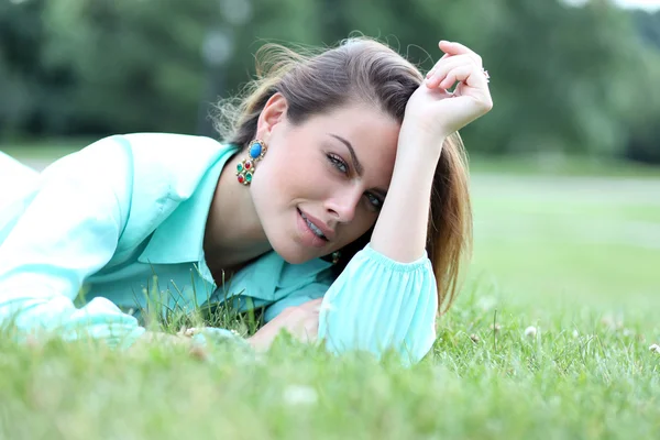 Portret van een jonge vrouw liggend op een groen gazon — Stockfoto
