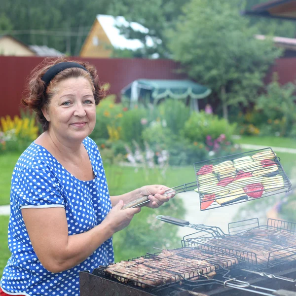 Mogen kvinna matlagning på en grill i trädgården — Stockfoto