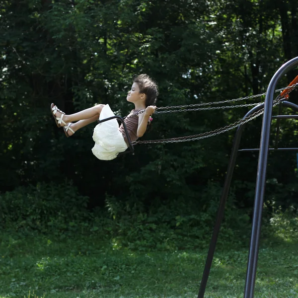 Menina feliz montando em um balanço no parque — Fotografia de Stock