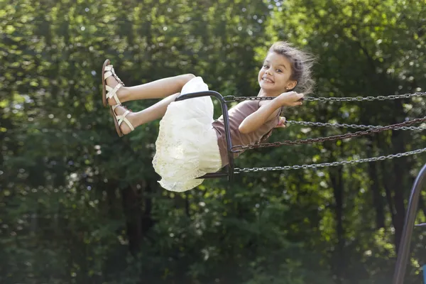 Glad liten flicka som rider på en gunga i parken — Stockfoto