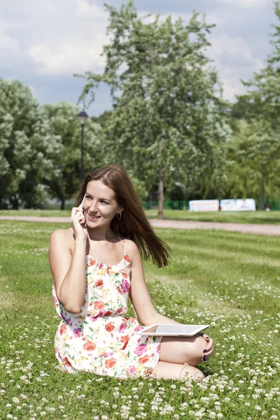 Mujer joven acostada en la hierba con el teléfono en la mano — Foto de Stock