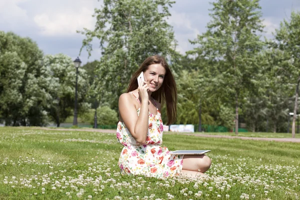 Genç bir kadın elinde telefon ile çim üzerinde yalan — Stok fotoğraf