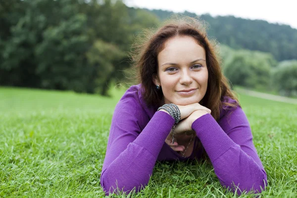 Jonge vrouw liggend op een groen gazon — Stockfoto