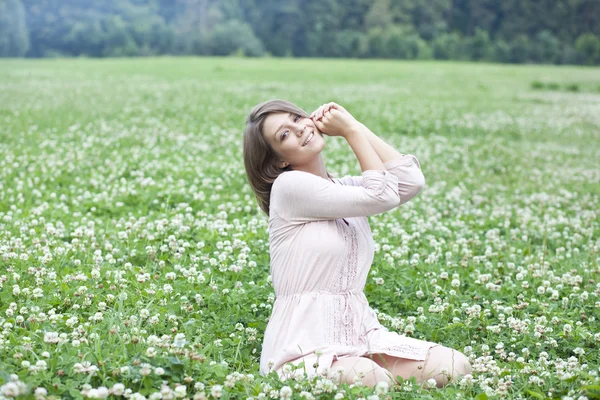 Ung kvinna sitter på en grön gräsmatta — Stockfoto