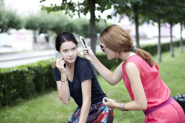 Leende unga flickor med mobiltelefon som satt på en bänk i en park — Stockfoto