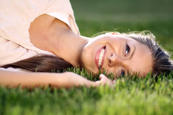 Jovem deitada em um gramado verde — Fotografia de Stock