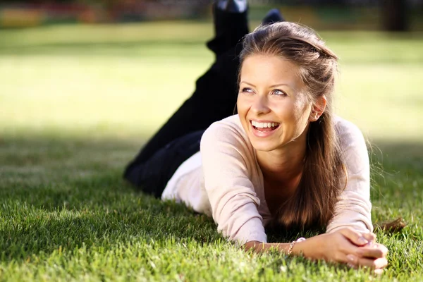 Portret van een jonge vrouw liggend op een groen gazon — Stockfoto