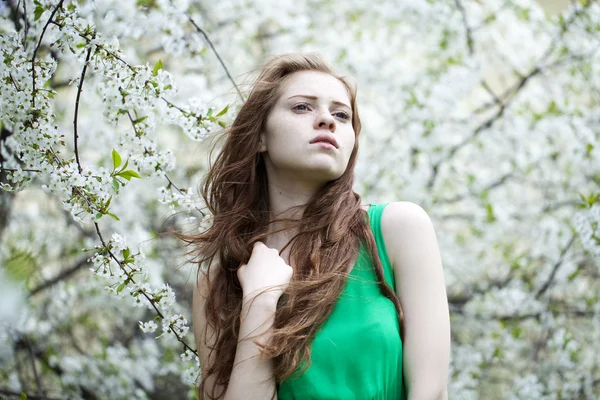 Vacker ung flicka står nära blommande träd i våren gard — Stockfoto