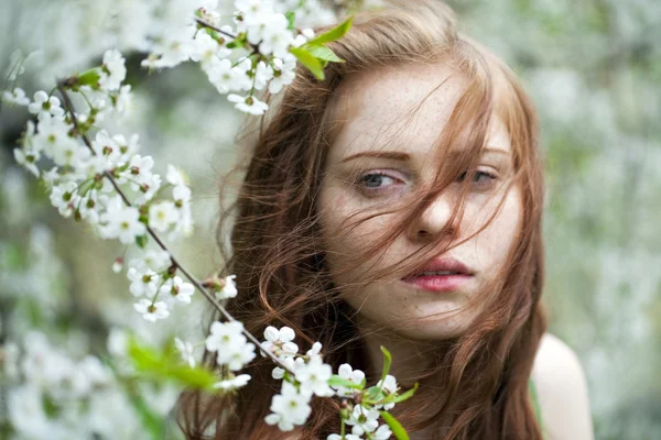 Schönes junges Mädchen, das neben blühenden Bäumen in der Frühlingsgarde steht — Stockfoto