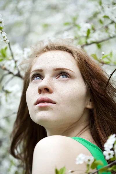 Vacker ung flicka står nära blommande träd i våren gard — Stockfoto