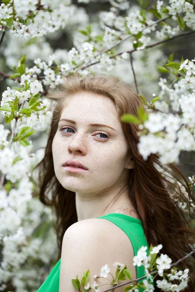 Beautiful young girl standing near blooming trees in spring gard — Stock Photo, Image