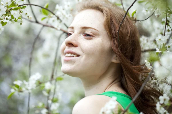 Vacker ung flicka står nära blommande träd i våren gard — Stockfoto