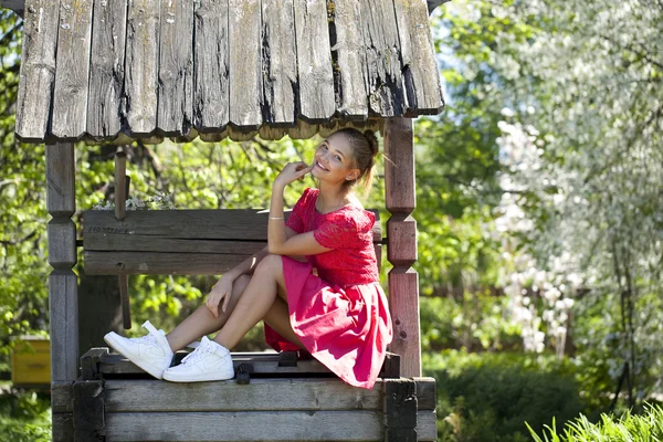 Schönes Mädchen sitzt auf einer Holzgrube im Park — Stockfoto