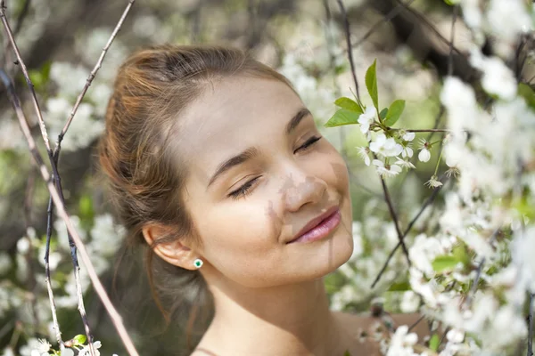 Vacker ung flicka står nära blommande träd i våren gard — Stockfoto